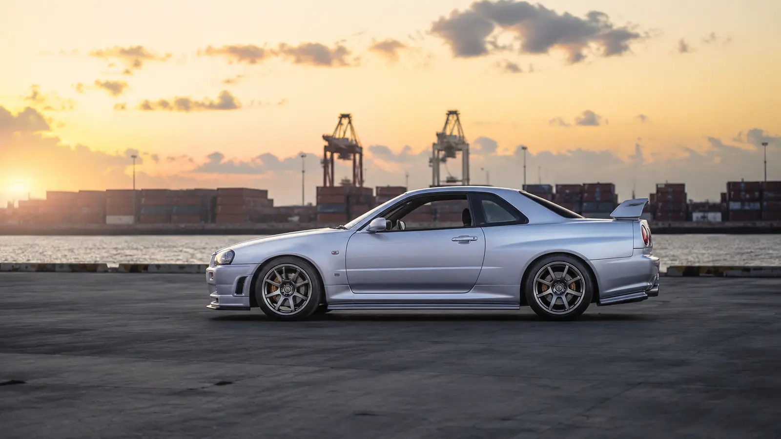АВТО 1000687 серебристый Nissan Skyline R34 в профиль в промышленной гавани